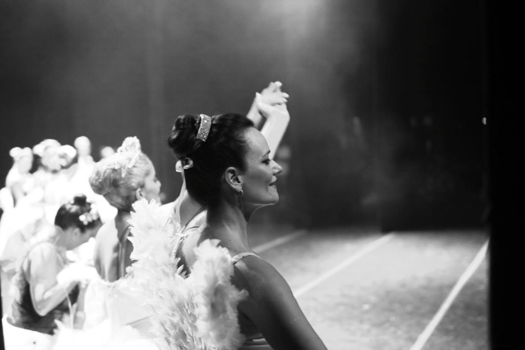Descrição da imagem #pracegover: A foto, em preto e branco, tem as bailarinas no encerramento de uma apresentação. Elas estão no palco e têm as mãos levantadas, em sinal de agradecimento do público. Fim da descrição.Fim da descrição.