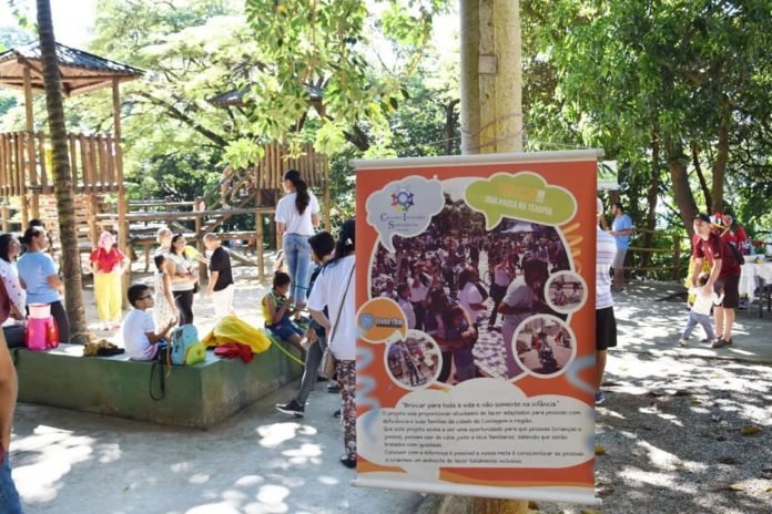 Descrição da imagem #pracegover: Uma das edições do piquenique inclusivo. Várias pessoas estão em um parque. Em primeiro plano está um banner do evento. Fim da descrição.