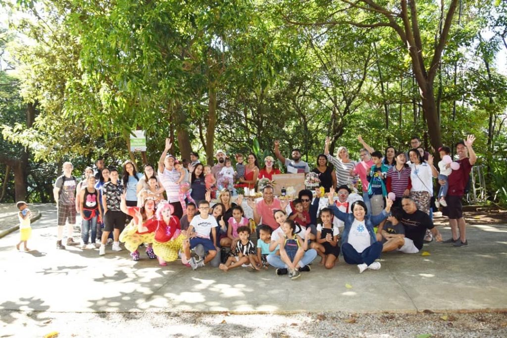 Descrição da imagem #pracegover: Os participantes do piquenique inclusivo. Várias pessoas estão juntas e posam para a foto em um parque. Ao fundo, vemos árvores. Fim da descrição.