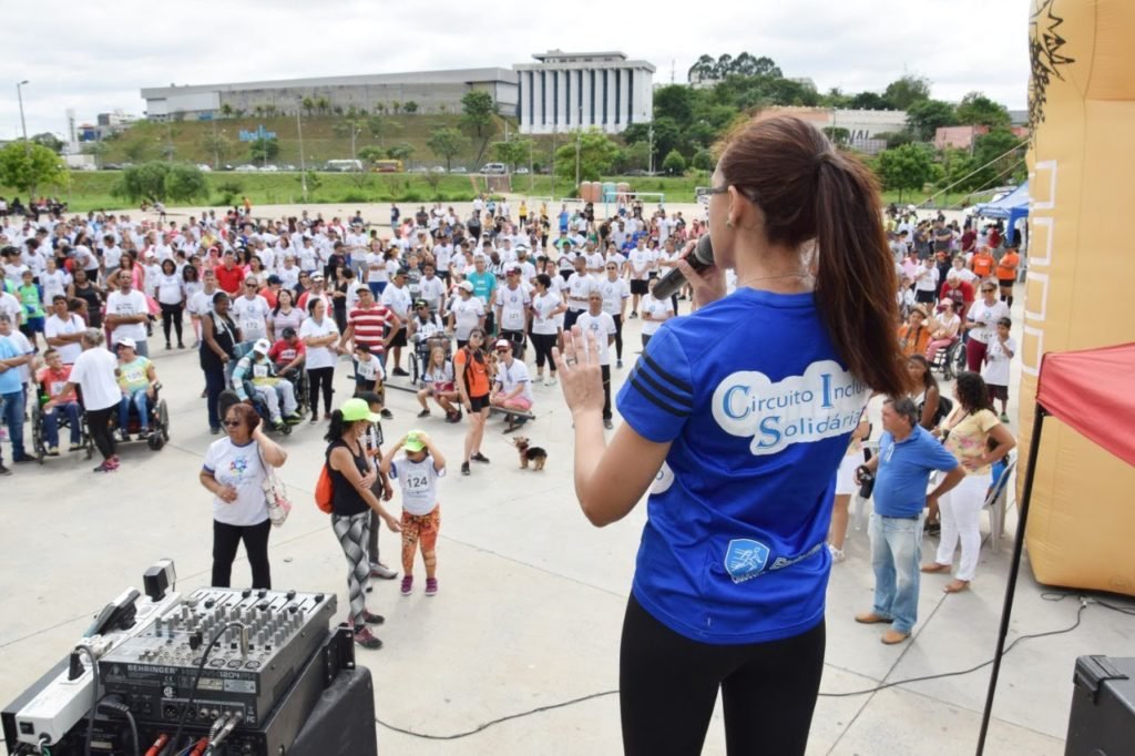 Descrição da imagem #pracegover: Uma mulher está no palco e fala para várias pessoas que olham para ela. Fim da descrição.