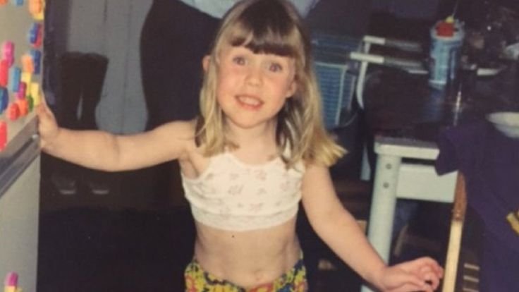 Descrição da imagem #pracegover: Eloise Stark durante a infância. Ela é uma menina loira e está usando um top bege. Fim da descrição.