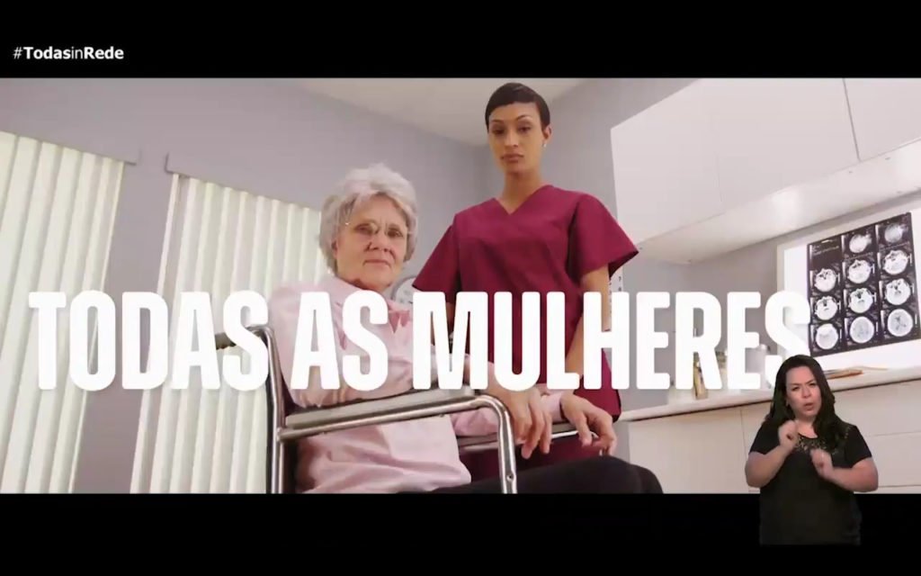 Descrição da imagem #pratodosverem: Reprodução do vídeo de divulgação do programa. Imagem de duas mulheres. Uma idosa cadeirante e uma enfermeira, que está ao seu lado. A imagem traz, escrito em letras brancas: TODAS AS MULHERES. No canto inferior direito está a intérprete de Libras e no canto superior esquerdo está o logo do programa: TODAS in-Rede. Fim da descrição.
