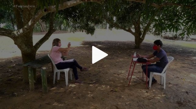 Descrição da imagem #pracegover: A professora Joyce e o aluno surdo Edilson, durante a aula. Eles estão sentados embaixo de uma árvore. Fim da descrição.