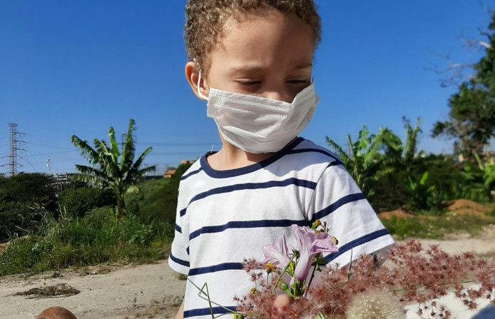 Descrição da imagem #pratodosverem: Um menino está montado no cavalo. Ele usa máscara e segura um ramo de folhagens do campo e flores. Fim da descrição.