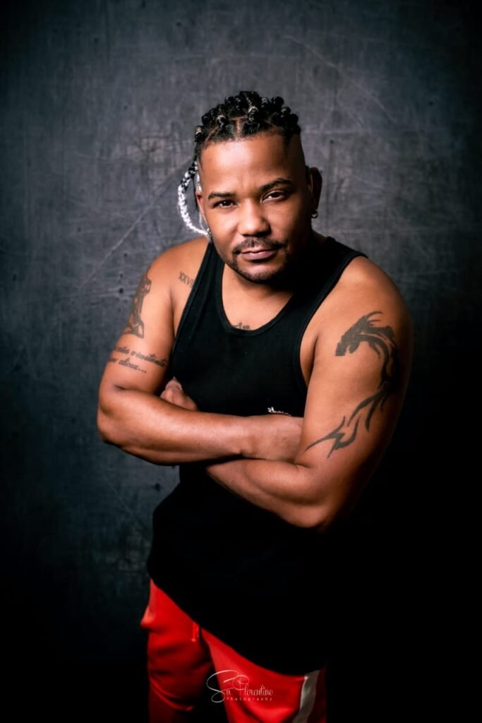 Descrição da imagem #pracegover: Foto do coreógrafo surdo Jhonny. Ele é um homem negro e tem cabelos longos, trançados. Jhonny usa uma regata preta e tem tatuagens nos braços. Fim da descrição.