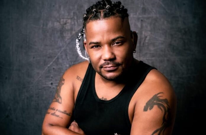 Descrição da imagem #pracegover: Foto do coreógrafo surdo Jhonny. Ele é um homem negro e tem cabelos longos, trançados. Jhonny usa uma regata preta e tem tatuagens nos braços. Fim da descrição.