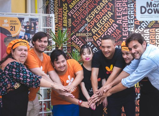Descrição da imagem #pracegover: Leonardo Gontijo e Dudu do Cavaco com a equipe do Instituto Mano Down. Eles estão lado a lado e seguram as mãos, uns dos outros. Fim da descrição.