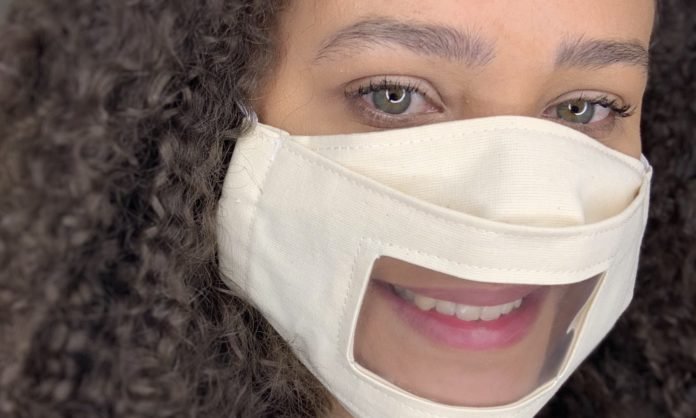Descrição da imagem #pratodosverem: Uma mulher está usando a máscara adaptada para surdos, que tem um visor transparente na parte da boca. Fim da descrição.