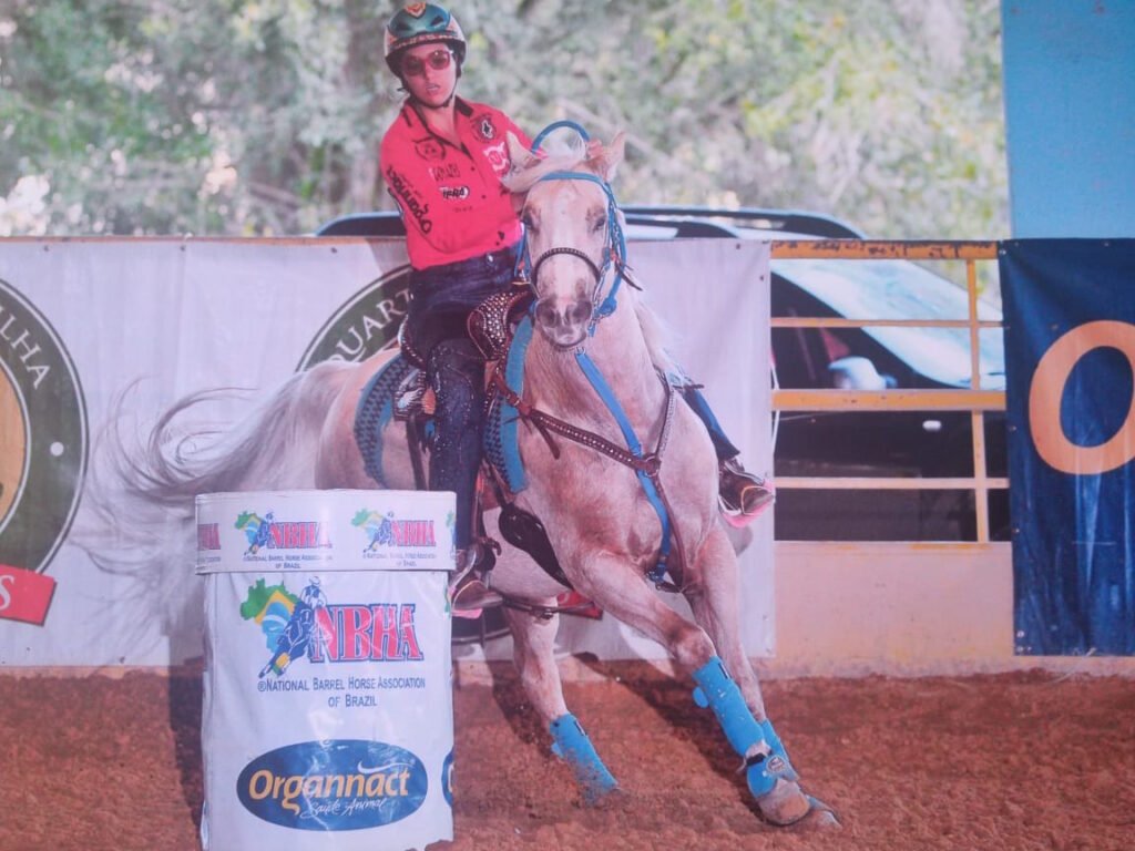 Descrição da imagem #pracegover: Veri está montada num cavalo durante o torneio de Três Tambores. Ela é uma moça morena e veste calça jeans e camisa pink. Fim da descrição.