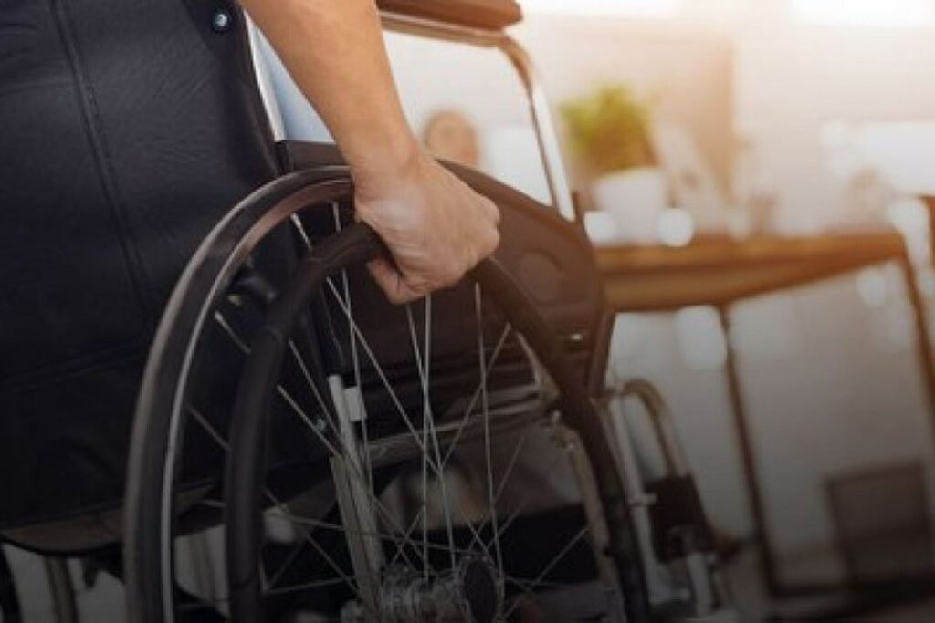 Descrição da imagem #pracegover: Foto de uma pessoa tocando sua cadeira de rodas. Vemos a mão de uma pessoa segurando na roda da cadeira. Fim da descrição.