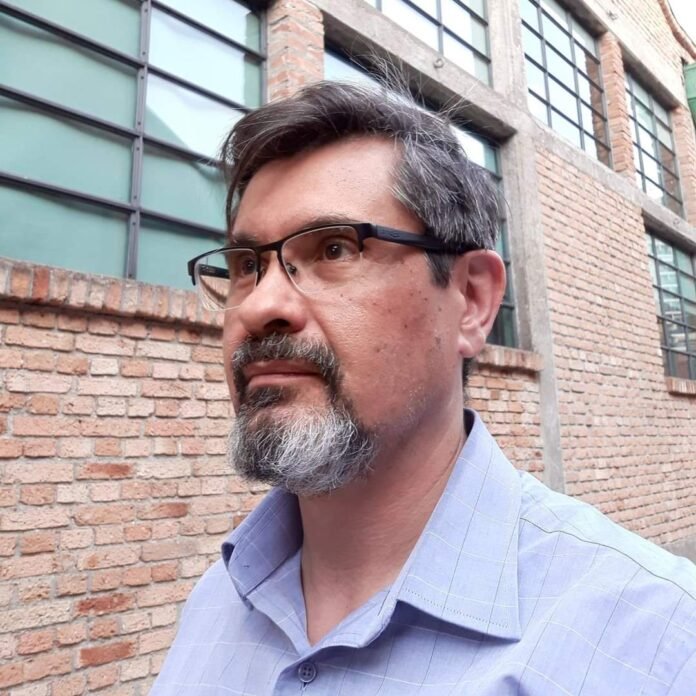Descrição da imagem #pracegover: Foto do doutor Roger, do CEJAM. Ele é um homem moreno, de cabelos e barba grisalha. Roger usa óculos e veste uma camisa azul. Fim da descrição.
