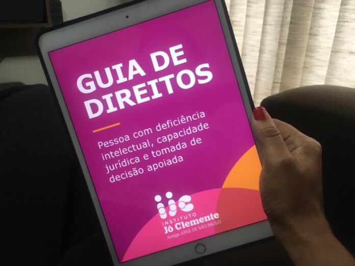 Descrição da imagem #pracegover: Uma mão está segudando um tablet. Na tela, está a capa do guia de direitos do Instituto Jô Clemente. Fim da descrição.