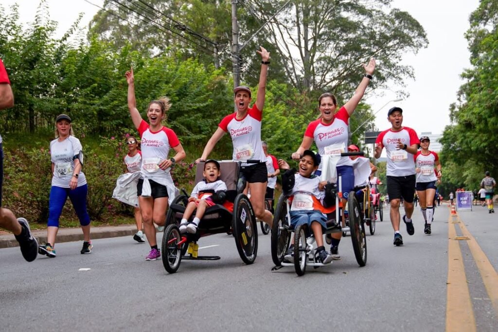 Descrição da imagem #pracegover: Foto de um grupo de corredores durante uma corrida, que teve a participação de pessoas com deficiência. Entre os corredores, vemos participantes em cadeiras de rodas. Eles estão com os braços levantados. Fim da descrição.