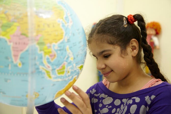 Descrição da imagem #pracegover: Foto de uma menina cega. Ela é morena e tem cabelos castanhos presos em trança. A menina está tocando um globo terrestre. Fim da descrição.