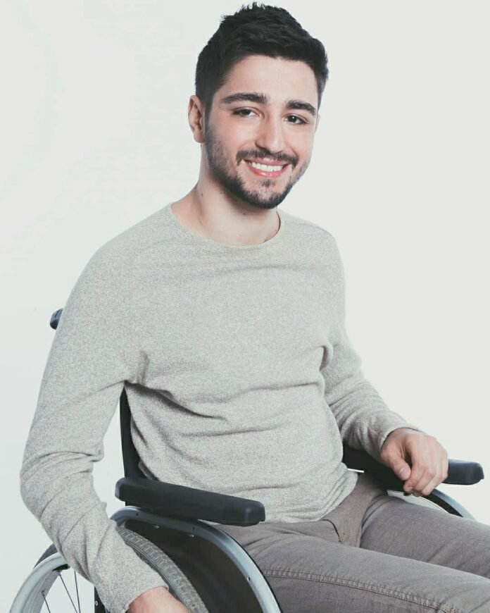 Descrição da imagem #pracegover: Foto de André Venturini. Ele é um homem moreno, de cabelos curtos e castanhos. André está vestindo uma blusa cinza de mangas compridas e está em sua cadeira de rodas. Fim da descrição.