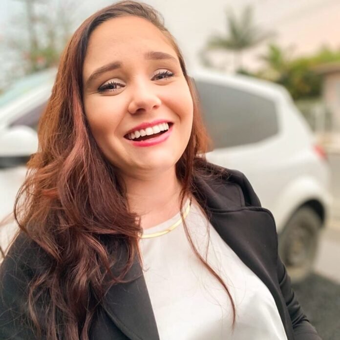 Descrição da imagem #pracegover: A jovem Bruna Salvador. Ela é uma mulher morena com cabelos castanhos lisos e compridos. Bruna está sorrindo. Ela usa uma blusa branca e um terninho preto. Fim da descrição.
