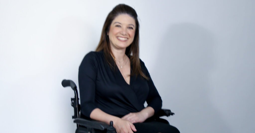 Descrição da imagem #pracegover: Luciana Trindade. Ela é uma mulher morena com cabeloss castanhos lisos e compridos. Luciana está sentada em sua cadeira de rodas e está usando um vestido preto. Fim da descrição.