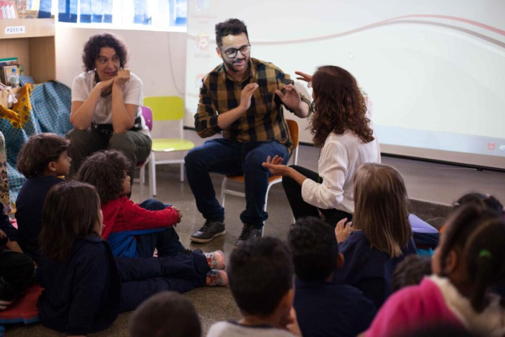 Descrição da imagem #pracegover: Foto de um evento da Mais Diferenças, em que os educadores promovem uma mediação de leitura acessível e inclusiva. Na imagem vemos várias criancas sentadas em roda acompanhando a mediação em Libras. Fim da descrição.