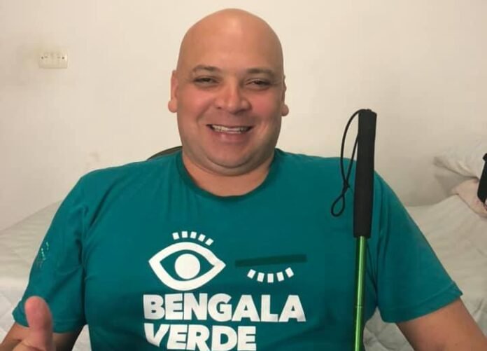 Descrição da imagem #pracegover: Foto de Sonny Pólito. Ele é um homem moreno e careca. Sonny está vestindo uma camiseta verde e nela está escrito, em letras brancas: Bengala Verde, com o logo que é formado por um olho. Sonny está sorrindo. Ele segura sua bengala com a mão esquerda. Fim da descrição.