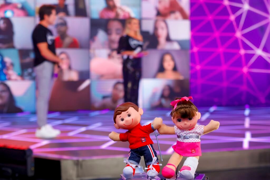 Descrição da imagem #pracegover: Foto do palco do Teleton 2020. Em primeiro plano vemos os bonecos do Tonzinho e da Nina. Ao fundo estão os padrinhos do Teleton, Daniel e Eliana. Fim da descrição.