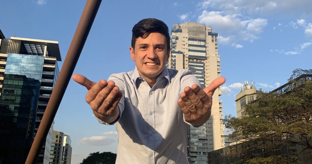 Descrição da imagem #pracegover: Foto de Vinícius Scheafer. Ele é um homem moreno, de cabelos curtos e castanhos. Vinícius está vestindo uma camisa social azul claro e faz o sinal de vem em Libras. Fim da descrição.