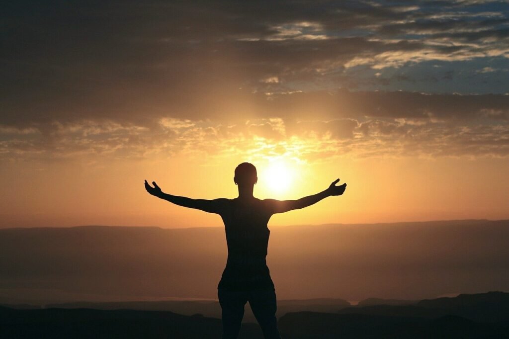 Descrição da imagem #pracegover: Imagem do pôr do sol. Vemos a silhueta de uma pessoa que está de braços abertos, em sinal de agradecimento. Fim da descrição.