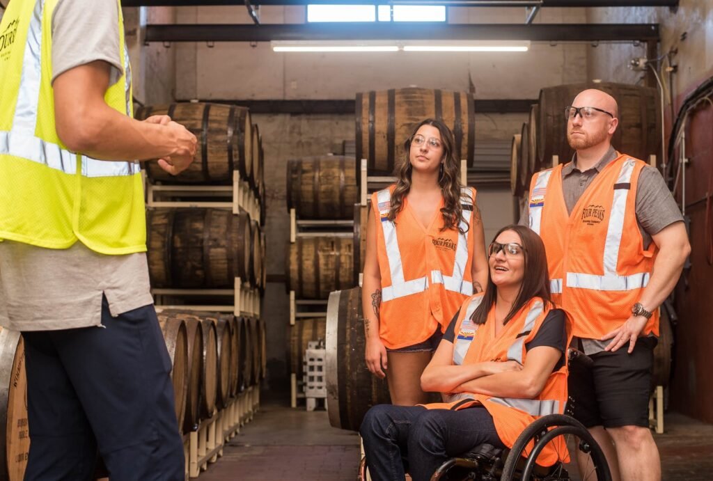 Descrição da imagem #pracegover: Foto de algumas pessoas acompanhando uma apresentação em uma empresa. Elas usam equipamentos de segurança, como jalecos e óculos de proteção. Entre as pessoas que assistem, está uma mulher cadeirante. Fim da descrição.
