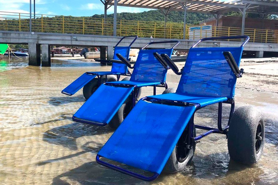 Descrição da imagem #pracegover: Foto das cadeiras anfíbias na praia da Ilha do Mel. Ela tem peneus largos e estrutura azul. Fim da descrição.