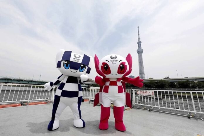 Descrição da imagem #pracegover: Foto dos mascotes das Olimpíadas e das Paralimpíadas de Tóquio. Eles são robôs e estão em um ponto turístico de Tóquio. O mascote das Olimpíadas é branco com detalhes em azul e a mascote das Paralimpíadas é branca com detalhes em cor de rosa. Fim da descrição.
