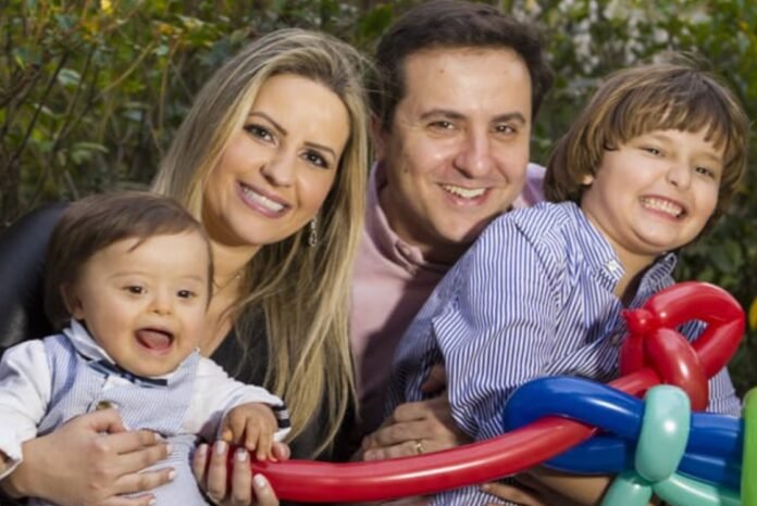 Descrição da imagem #pracegover: Foto de um homem e uma mulher com duas crianças. Uma das crianças tem síndrome de Down. Todos estão sorrindo. Fim da descrição.