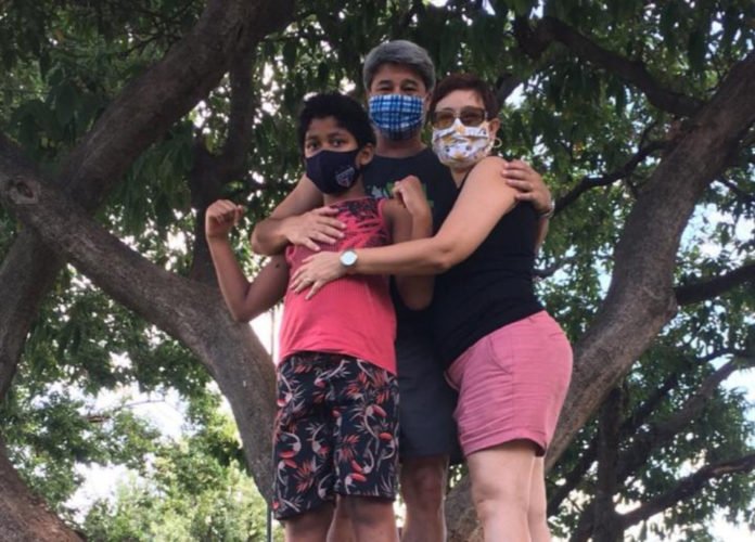 Descrição da imagem #pracegover: Foto do Gabriel com a mamãe Ana Iris e o papai Marcelo. Eles estão em um parque e se abraçam. Fim da descrição.