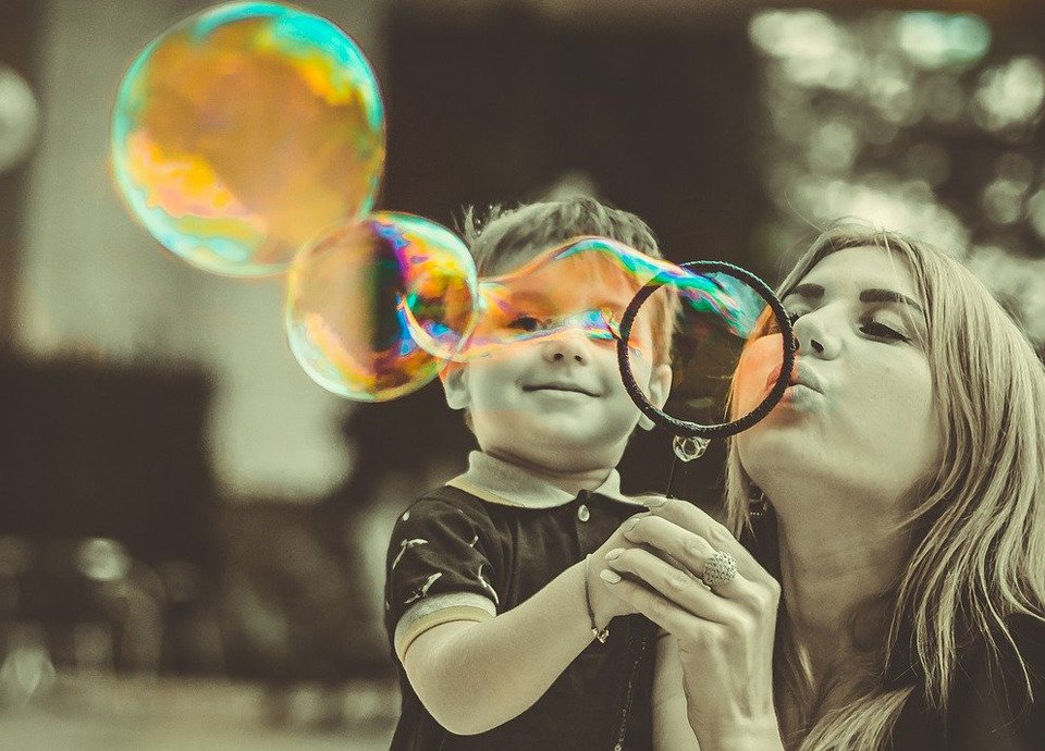 Descrição da imagem #pracegover: Foto de uma mulher com um menino. Eles estão brincando de fazer bolhas de sabão no ar. Fim da descricão.