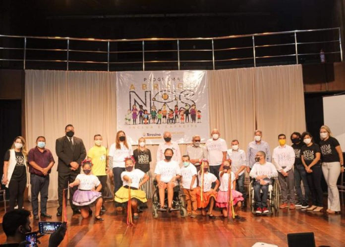 Descrição da imagem: Foto de todos os participantes durante o lançamento do programa Abrace Nós. As pessoas estão lado a lado, no palco do evento.Fim da descrição.