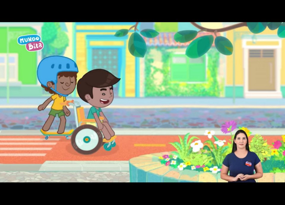 Descrição da imagem: Imagem do clipe. Na arte, duas crianças estão brincando. Uma delas está empurrando a cadeira de rodas do amigo. No canto inferior esquerdo está a intérprete de Libras. Fim da descrição.