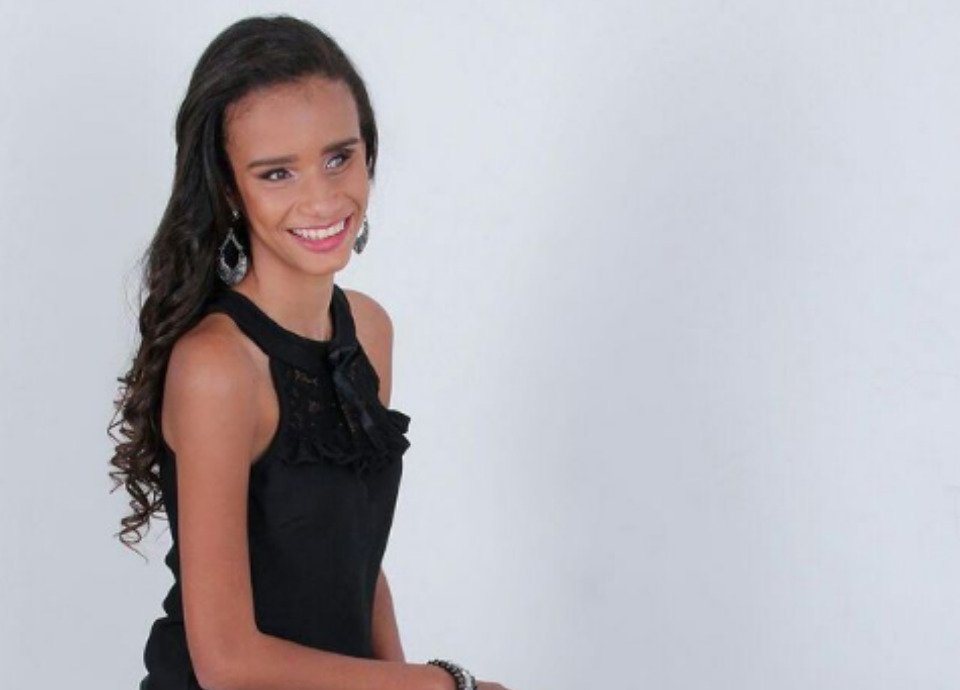 Descrição da imagem: Foto da Thaís Vitória. Ela é jovem, tem cabelos castanhos, lisos e compridos. Thaís está posando para a foto. Ela sorri. Fim da descrição.