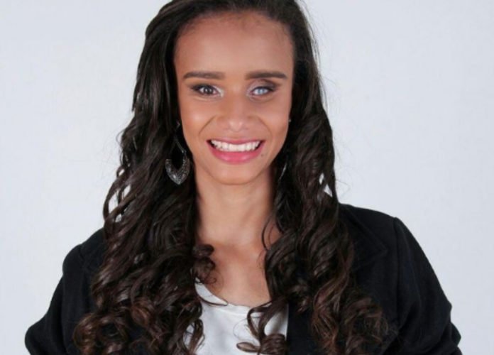Descrição da imagem: Foto de close da Thaís Vitória. Ela é jovem, tem cabelos castanhos, lisos e compridos. Thaís está sorrindo para a foto. Fim da descrição.