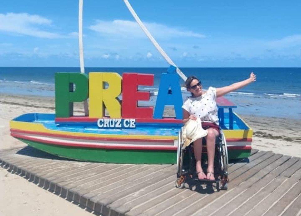 Descrição da imagem: Foto de Pamela. Ela está em sua cadeira de rodas. Pamela é um mulher loira, de cabelos lisos na altura dos ombros. Fim da descrição.
