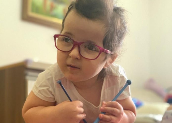 Descrição da imagem: Foto de Isabela. Ela é uma menina branca, de cabelos castanhos e usa óculos com armação vermelha. Fim da descrição.