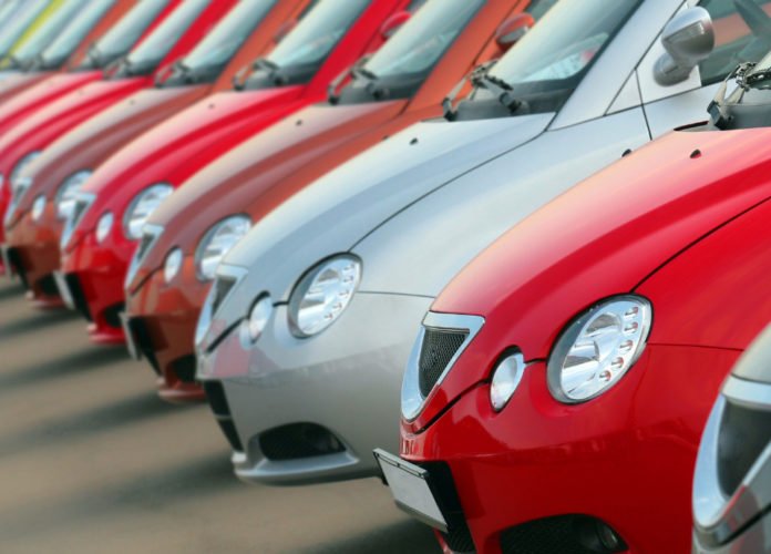 Descrição da imagem: Foto de vários carros enfileirados. Os carros são vermelhos e, um deles, é cinza. Fim da descrição.