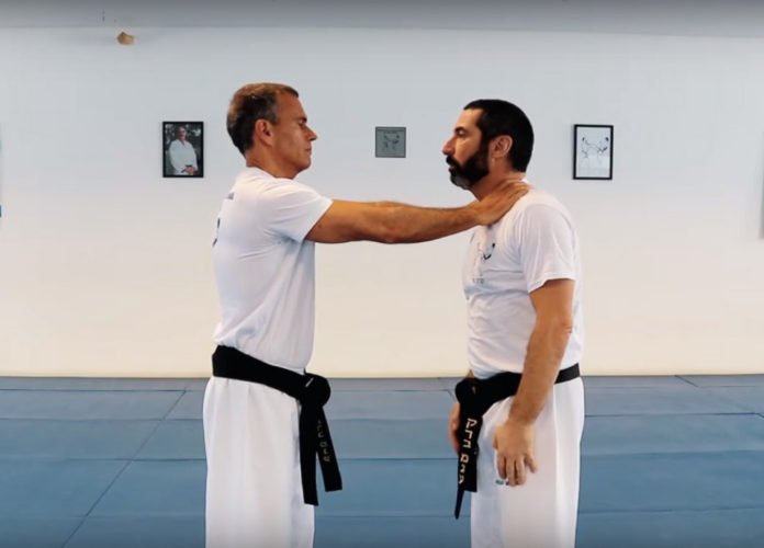 Descrição da imagem: Foto de dois homens durante um treino de Krav Magá. Eles estão frente a frente e usam roupas brancas e uma faixa preta na cintura. Fim da descrição.