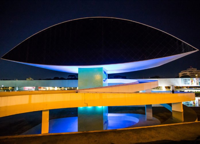 Descrição da imagem: Foto do Museu Oscar Niemeyer iluminado de azul. Fim da descrição.