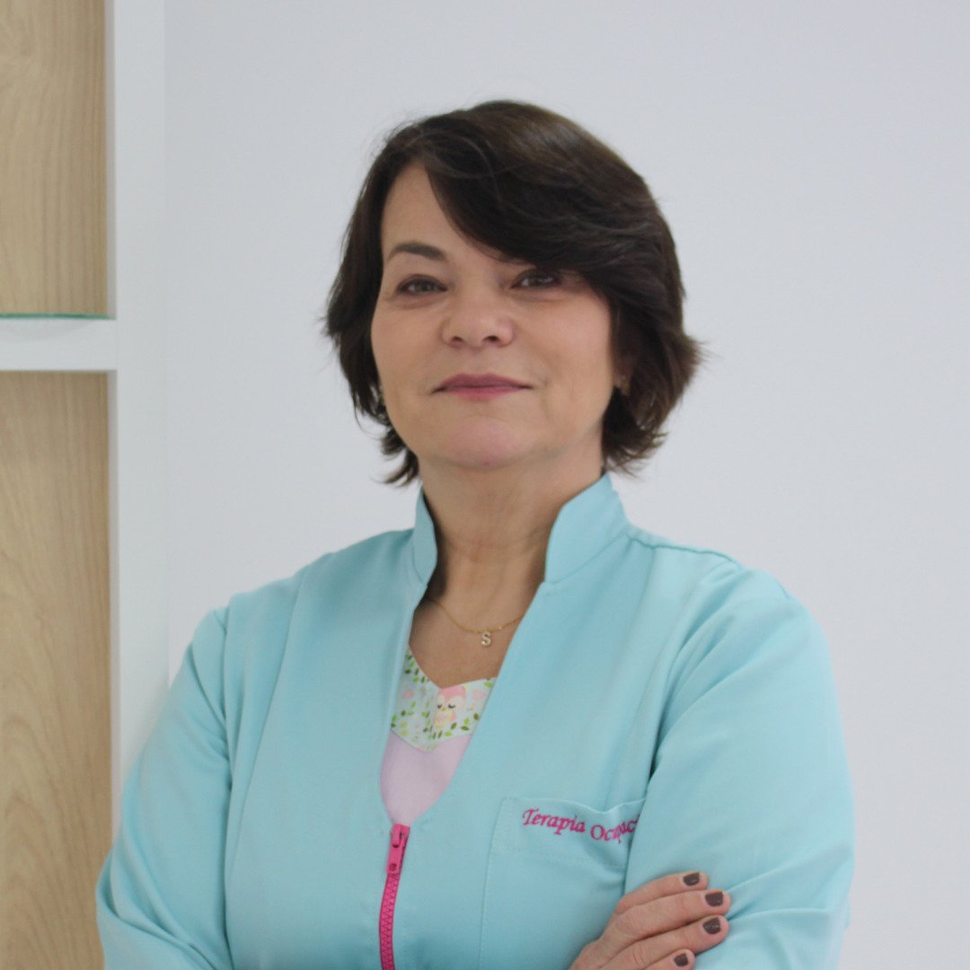 Descrição da imagem: Foto da Syomara. Ela é uma mulher de pele branca, cabelos pretos, curtos. Syomara está vestindo uma camisa azul clara e está com os braços cruzados. Fim da descrição.