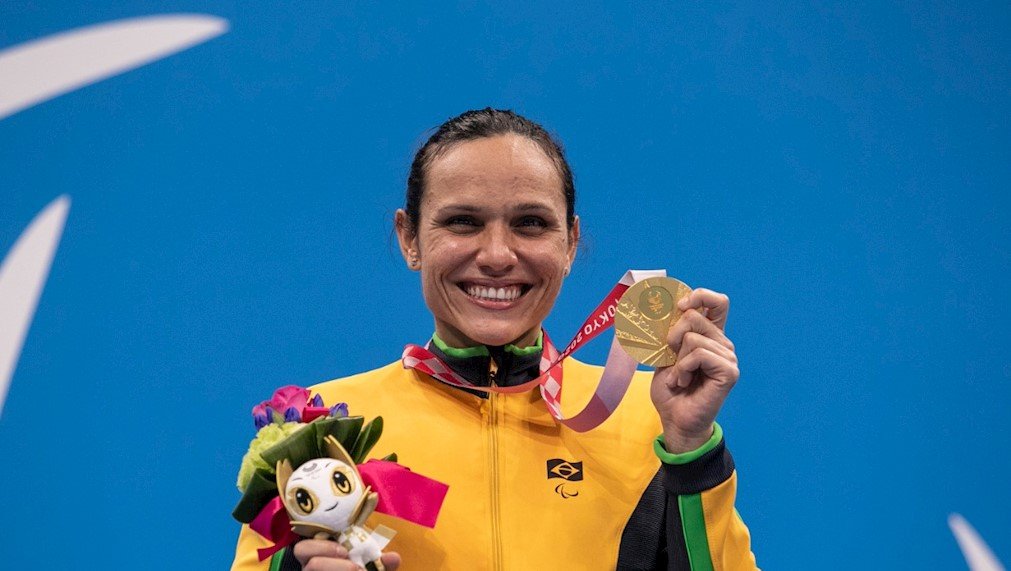 Descrição da imagem: Foto da atleta Carol Santiago. Ela está segurando sua medalha de ouro. Fim da descrição.