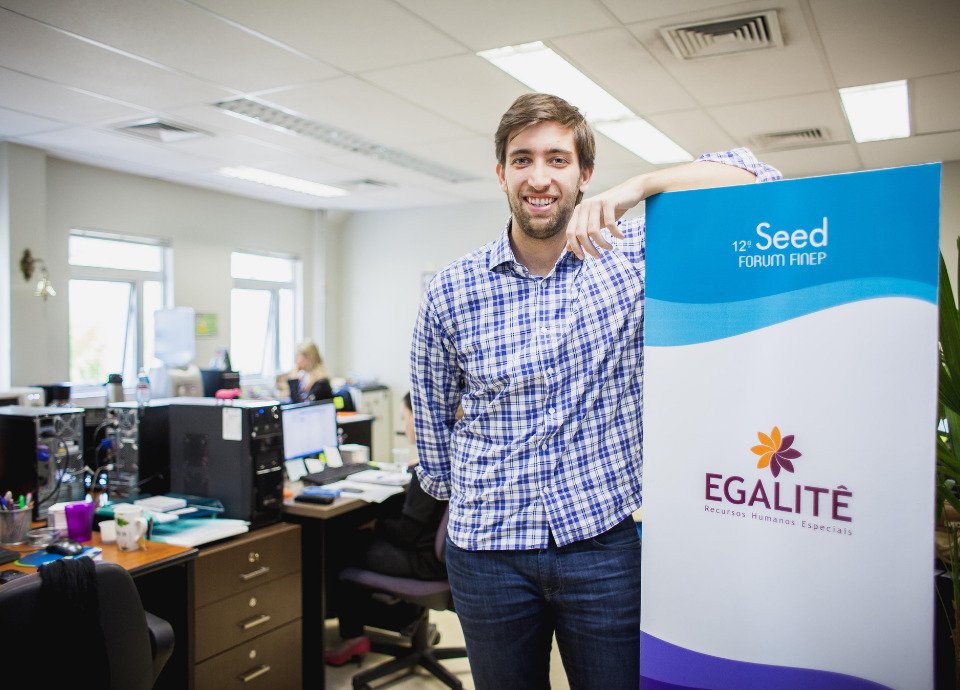 Descrição da imagem: Foto de Guilherme Braga, CEO da Egalitê. Ele é um homem branco e está em um escritório, ao lado de um banner da Egalitê. Fim da descrição.