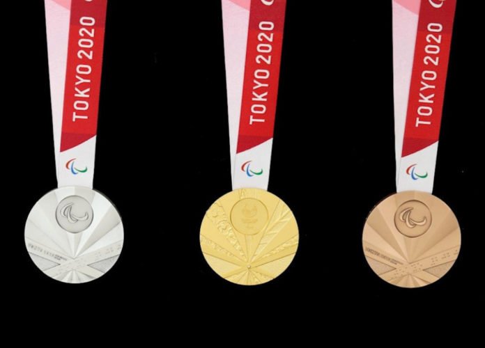 Descrição da imagem: Foto das medalhas de ouro, prata e bronze. Elas têm escritos em braille. Fim da descrição.