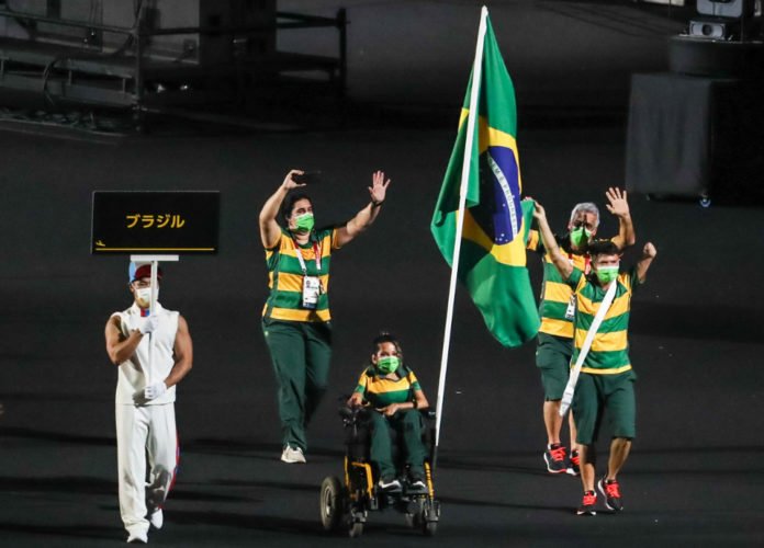 Descrição da imagem: Foto dos brasileiras durante a abertura dos Jogos. Eles estão carregando a bandeira do Brasil. Fim da descrição.