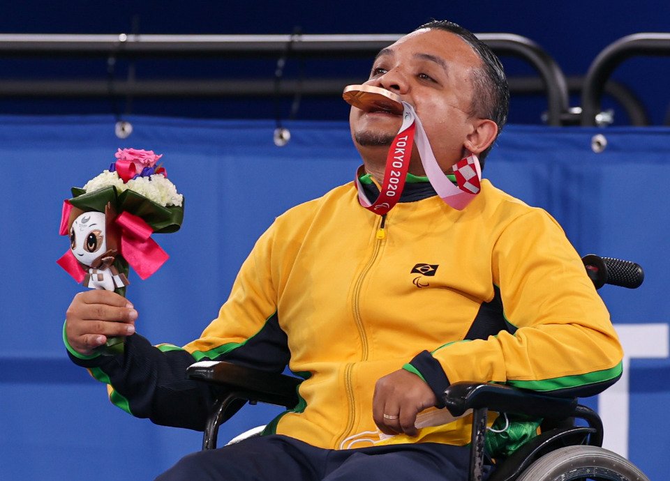 Descrição da imagem: Foto do atleta Maciel de Souza. Ele está com a medalha na boca. Fim da descrição.