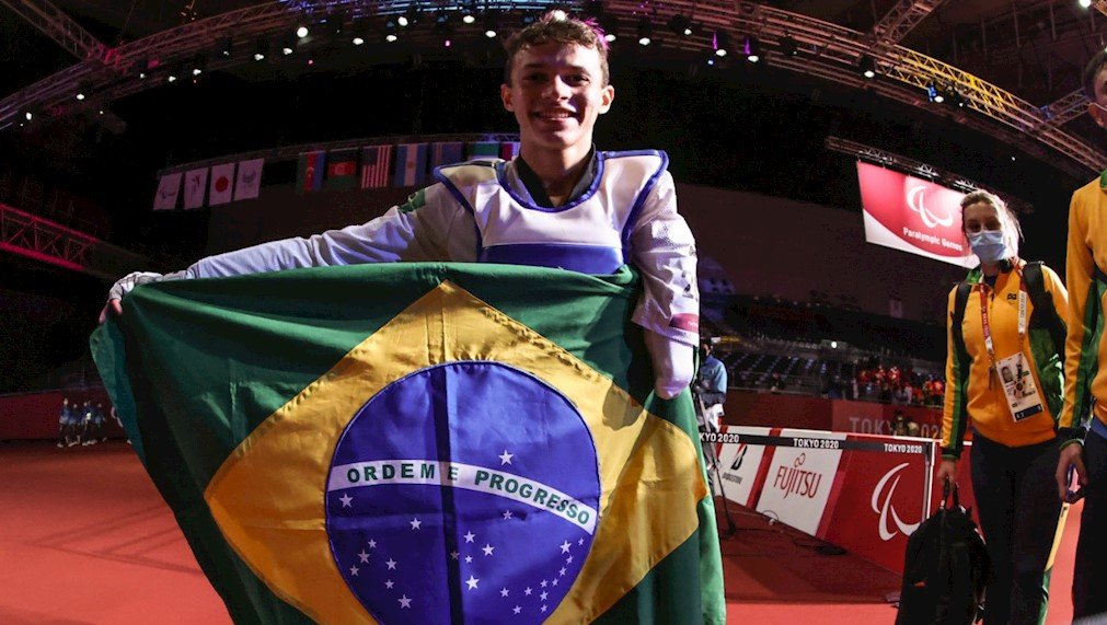 Descrição da imagem: Foto do atleta Nathan Torquato. Ele está segurando a bandeira do Brasil. Fim da descrição.
