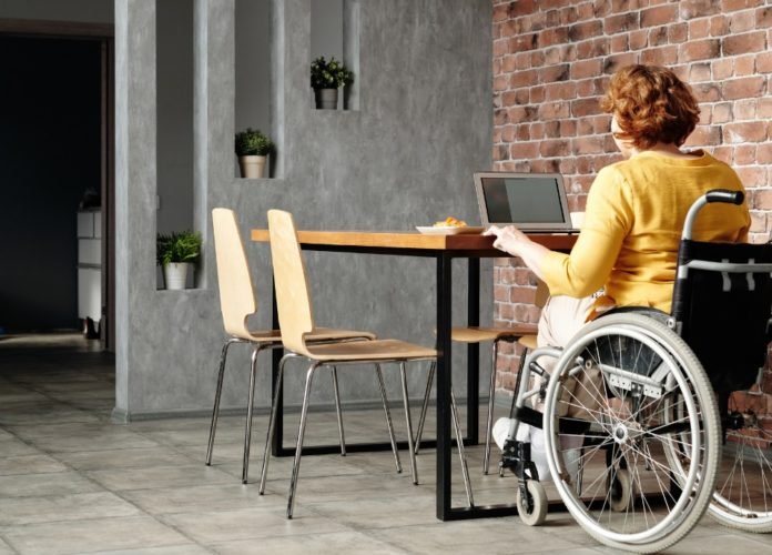 #descriçãodaimagem: Foto de uma jovem cadeirante trabalhando. Ela está usando um computador. Fim da descrição.
