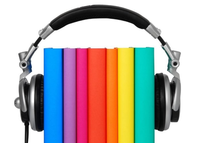 #descriçãodaimagem: foto de um fone de ouvidos preso a sete livros com capas coloridas. Fim da descrição.